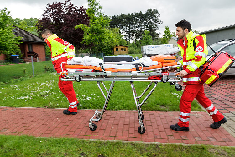 Zwei junge DRK-Mitarbeiter schieben eine Trage